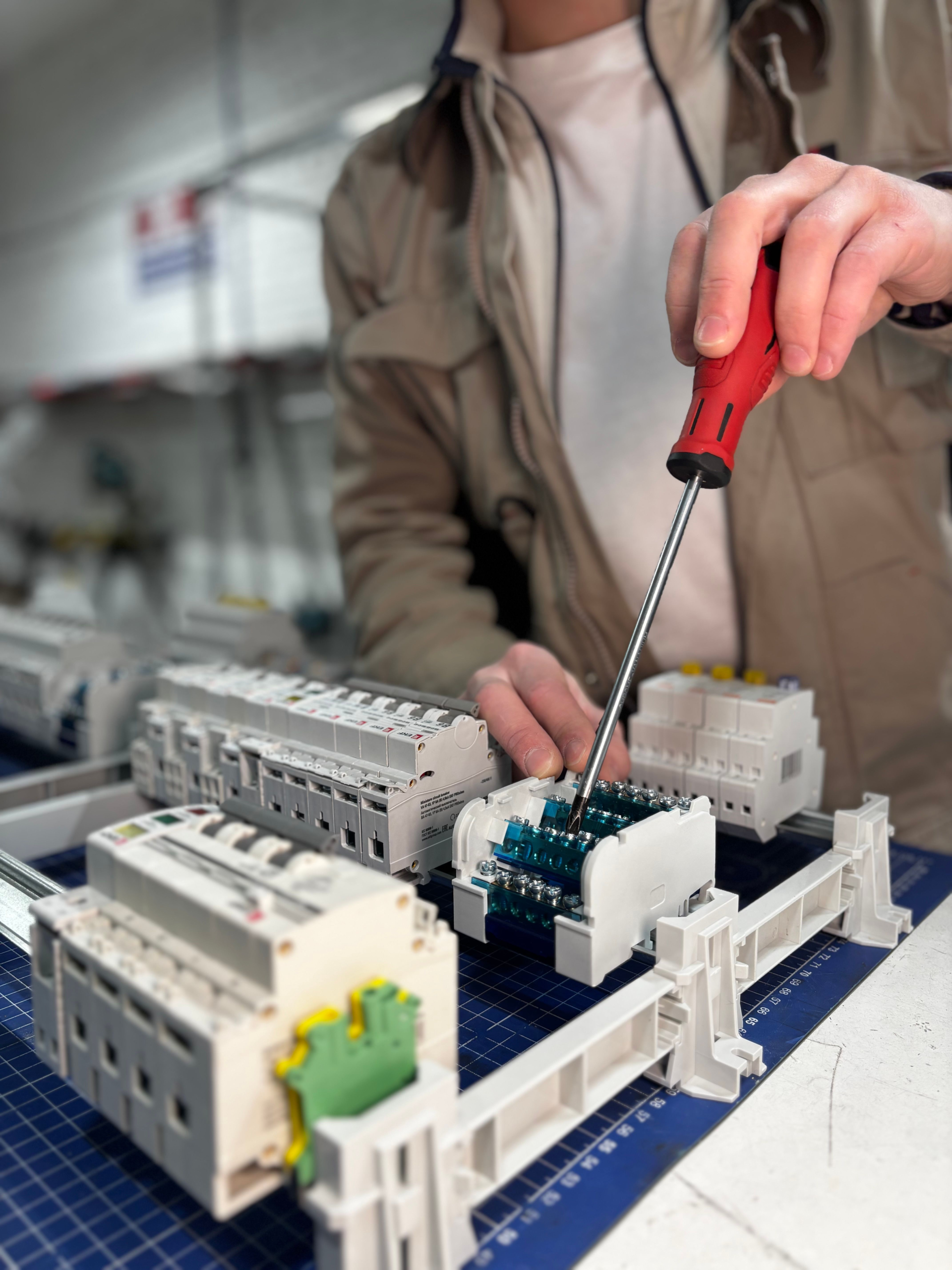 Técnico ajustando componentes eléctricos y bloques de terminales con un destornillador en un taller.